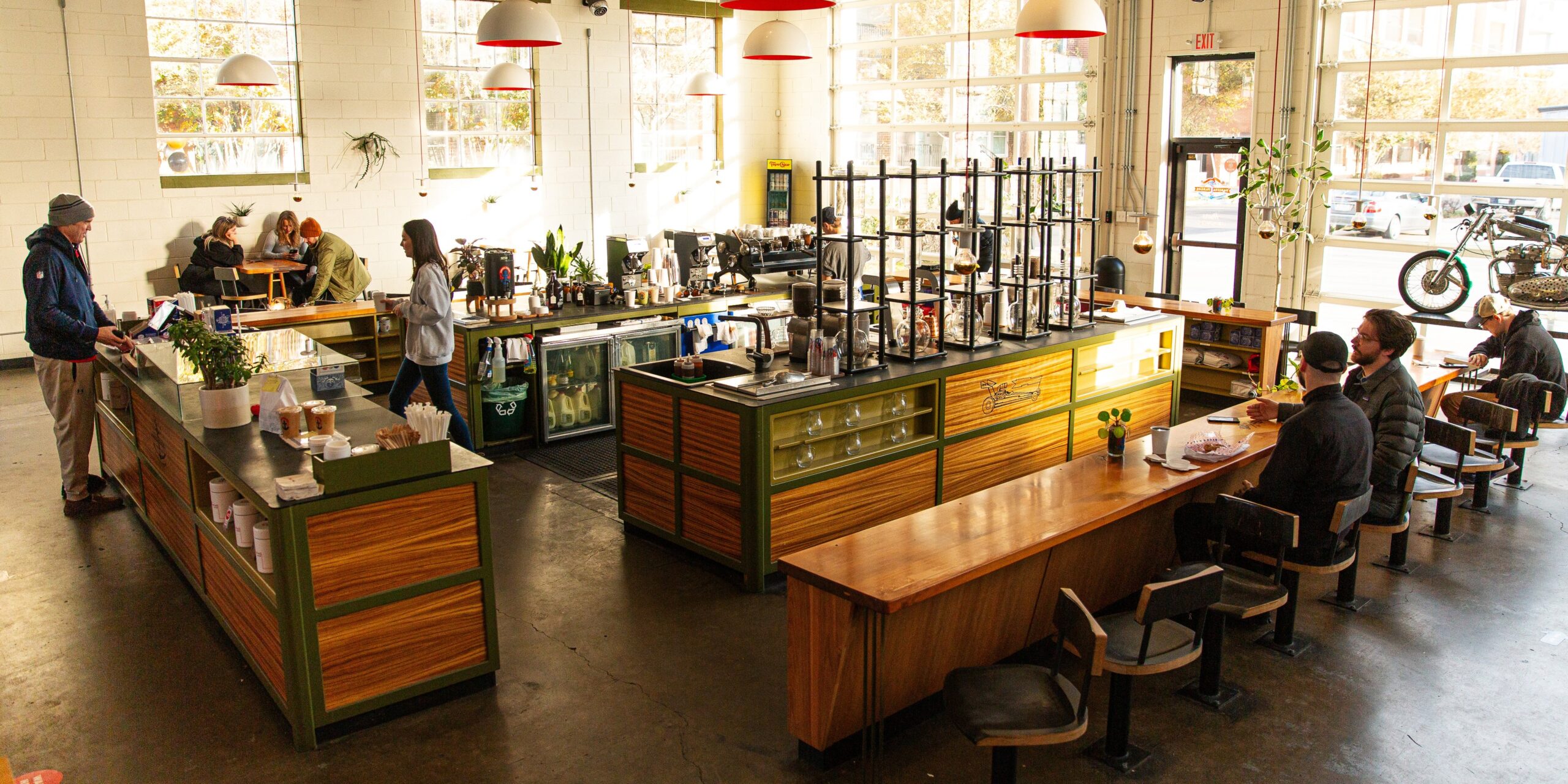 People are sitting at a coffee bar while someone orders at the counter.